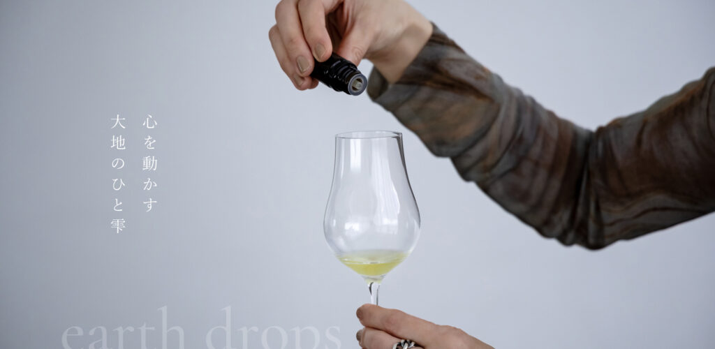 ワイングラスに精油を滴下しているところ 「心を動かす 大地の一雫 -earth drops」