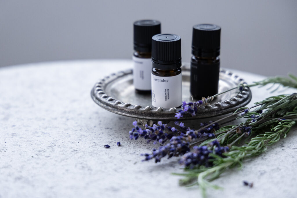 机の上に小皿に乗った精油が３本とラベンダーの花