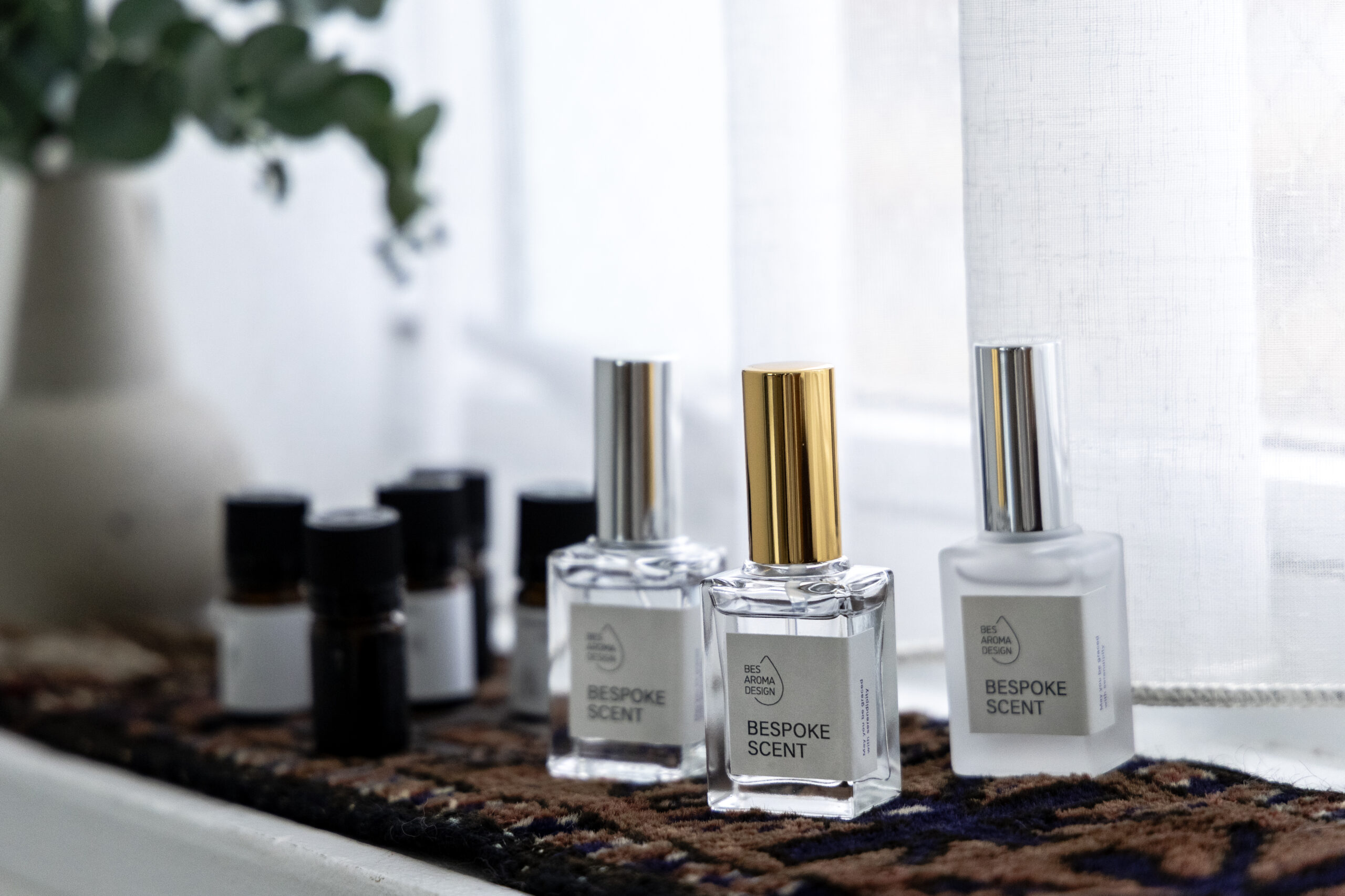 窓際に３本のガラスの香水瓶と数本の 精油